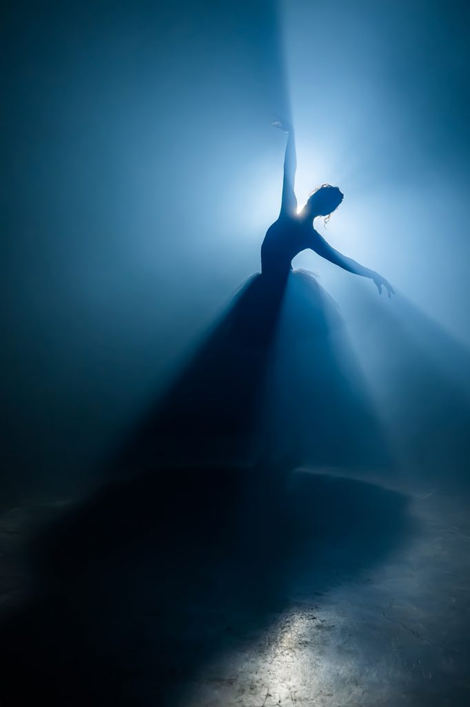 Solo performance by ballerina in tutu dress against backdrop of luminous neon spotlight in theater